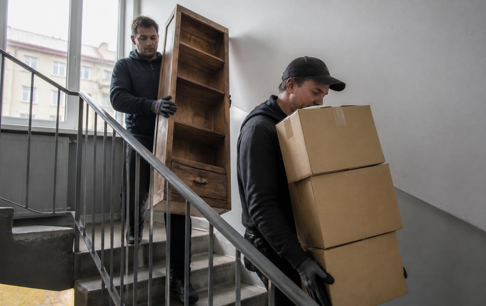 Kaks töömeest kannavad kolimisest üle jäänud kastid ja vana puidust riiuli kortermaja trepikojast alla