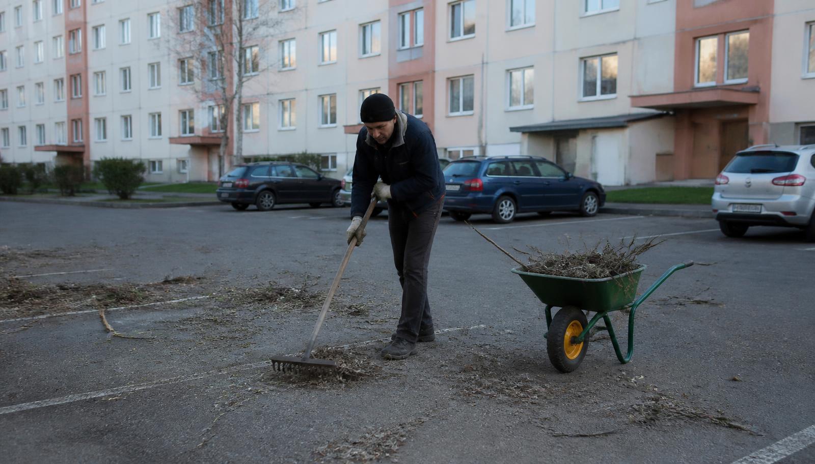 Töömees reha ja prahi ning okstega korterelamu parklas